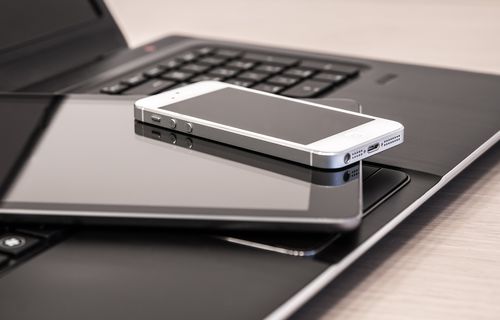 Technische Geräte liegen übereinander, darunter ein Laptop, ein Tablet und ein Handy.