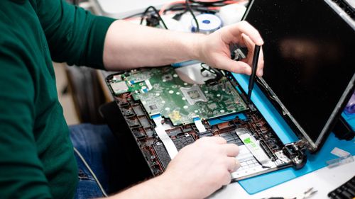 Eine Hand repariert einen aufgeschraubten Laptop.