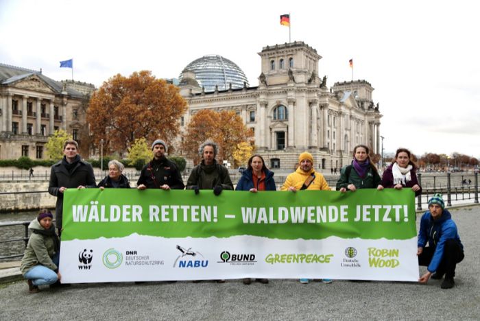 Menschen halten ein Transparent mit der Aufschrift "Waldwende jetzt" vor dem Bundestag in die Höhe. 