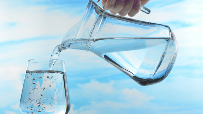 Eine Hand kippt Wasser aus einem Krug in ein Glas.