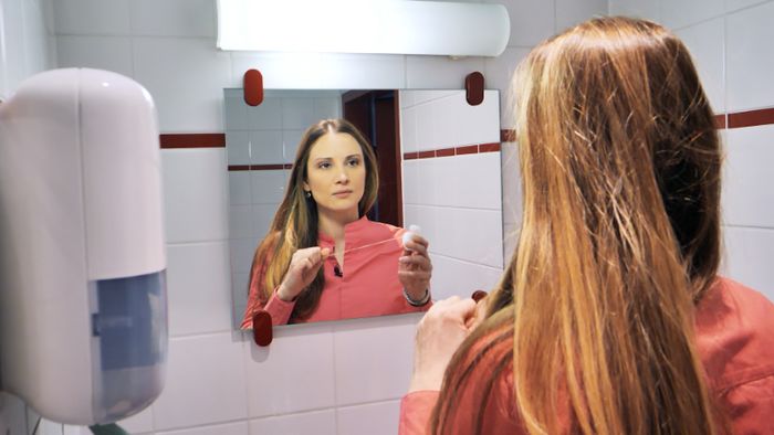 Eine Frau steht mit Zahnseide vor einem Badezimmerspiegel. 
